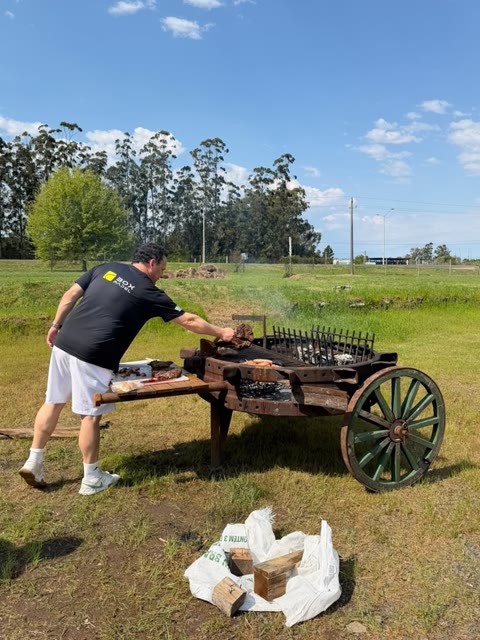 Asado en una parrilla de carreta sobre el pasto, al lado del galpón.
